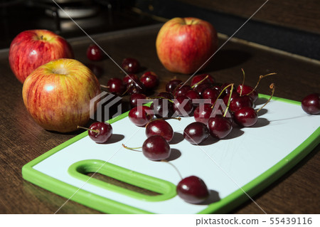 Apples and cherries on a cutting board. 55439116