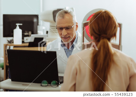 Grey-haired eye therapist talking to his patient Grey-haired eye therapist talking to his patient 55439123