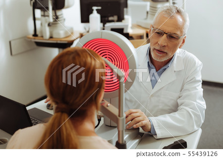 Professional ophthalmologist consulting young red-haired woman Professional ophthalmologist consulting young red-haired woman 55439126
