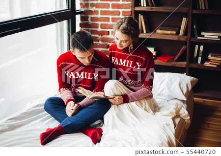 Couple in red sweaters reading book in bed 55440720