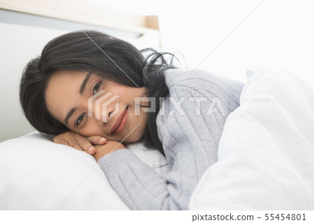Asian woman lies on one side on bed in bedroom.. Asian woman lies on one side on bed in bedroom.. 55454801