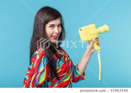Portrait of a smiling young woman with a vintage yellow video camera in her hands posing against a 55463544