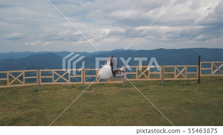 Groom with bride sit on the fence near mountain hills. Aerial drone shot 55463875