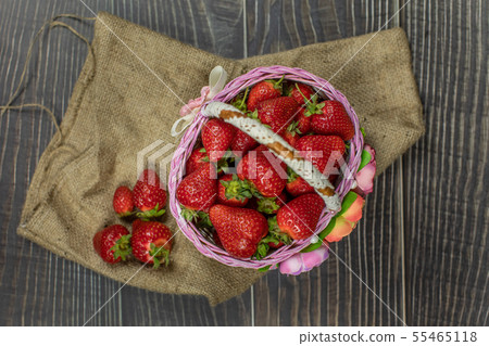 Strawberries in a small basket on the wooden table. 55465118