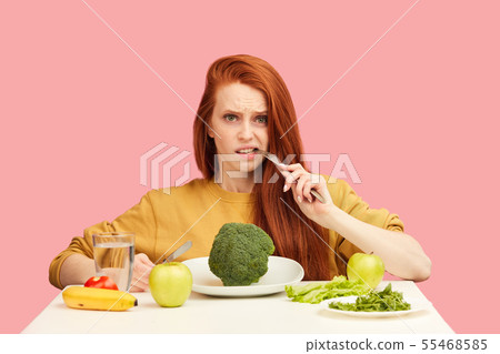 Vegetable diet. Sad dull woman holding broccoli on fork while making grimace Vegetable diet. Sad dull woman holding broccoli on fork while making grimace 55468585