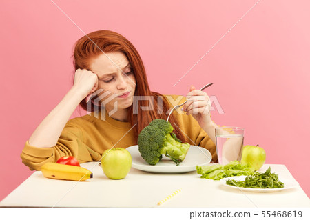 Vegetable diet. Sad dull woman holding broccoli on fork while making grimace 55468619