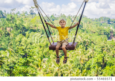 Young boy swinging in the jungle rainforest of Bali island, Indonesia. Swing in the tropics. Swings 55469371