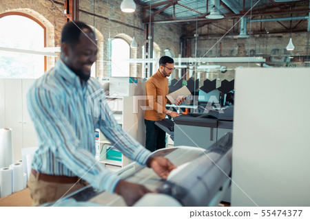 Smiling dark-skinned man working with colleague in publishing office Smiling dark-skinned man working with colleague in publishing office 55474377