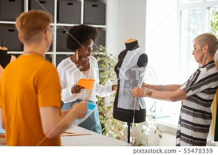 Tailor holding a tablet looking at her coworker 55478339