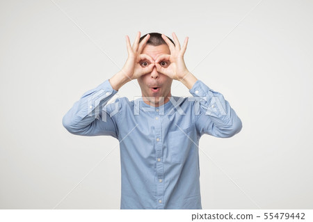 Young latin man showing owl sign with fingers. Young latin man showing owl sign with fingers. 55479442