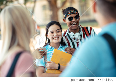 Cheerful boy hugging his girlfriend in front of his friends. Cheerful boy hugging his girlfriend in front of his friends. 55481199