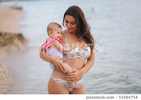 Portrait of Mother hold baby girl on hands on the beach in the sea. Mom and daughter in swimsuit 55484754