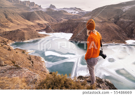 Portrait from the back of the girl traveler photographer in an orange sweater and hat with a camera 55486669