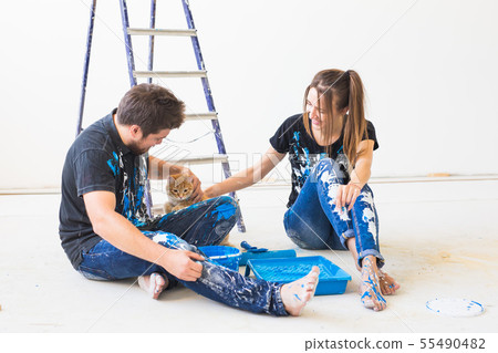 Pet, redecoration and relationship concept - Young funny couple with cat doing renovation in new 55490482