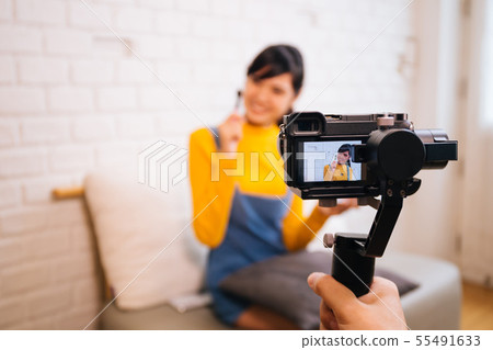 Young Asian woman holding cosmetics brush while recording a video with professional camera Young Asian woman holding cosmetics brush while recording a video with professional camera 55491633
