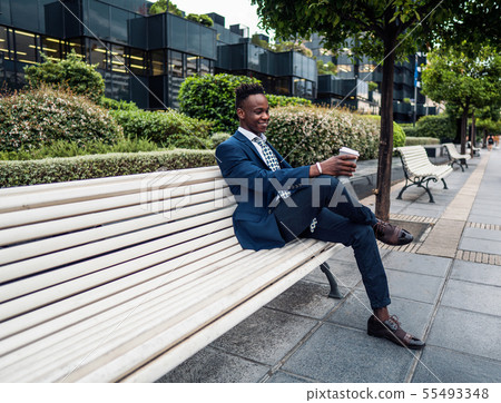 African American businessman wearing blue suit drinks coffee near office 55493348