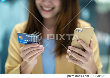Closeup Asian woman using credit card with mobile for online shopping in department store over the clothes shop store background, technology money wallet and online payment concept, credit card mockup Closeup Asian woman using credit card with mobile for online shopping in department store over the clothes shop store background, technology money wallet and online payment concept, credit card mockup 55504058