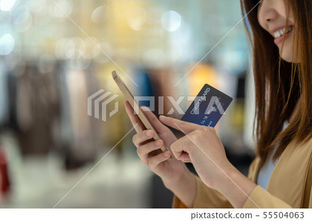 Closeup Asian woman using credit card with mobile for online shopping in department store over the clothes shop store background, technology money wallet and online payment concept, credit card mockup Closeup Asian woman using credit card with mobile for online shopping in department store over the clothes shop store background, technology money wallet and online payment concept, credit card mockup 55504063