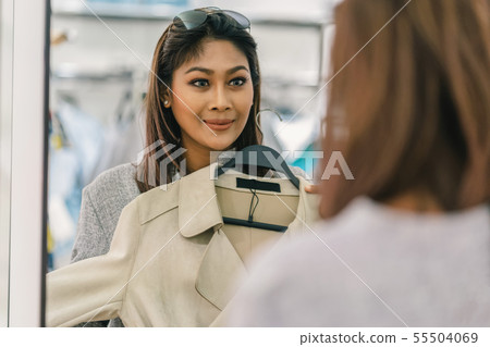 Happy Asian woman choosing clothes with reflection of glass in store shop with happy action at department center Happy Asian woman choosing clothes with reflection of glass in store shop with happy action at department center 55504069