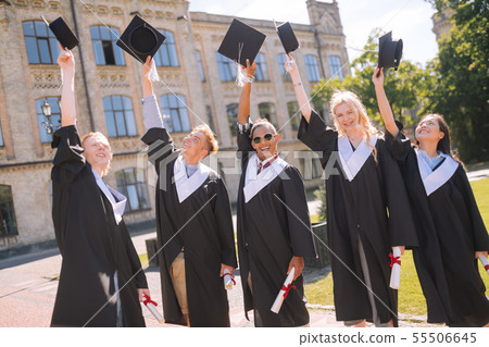 Cheerful graduates raising their masters caps in the air. Cheerful graduates raising their masters caps in the air. 55506645
