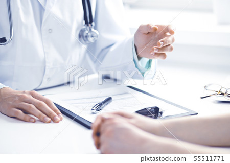 Doctor and female patient sitting at the desk and talking in clinic near window. Medicine and health Doctor and female patient sitting at the desk and talking in clinic near window. Medicine and health 55511771