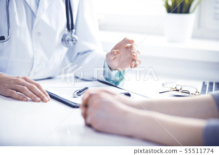 Doctor and female patient sitting at the desk and talking in clinic near window. Medicine and health 55511774