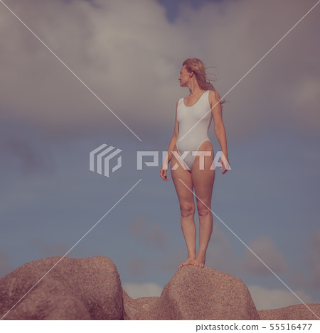 Woman in a white bathing suit on a stone by the se Woman in a white bathing suit on a stone by the se 55516477