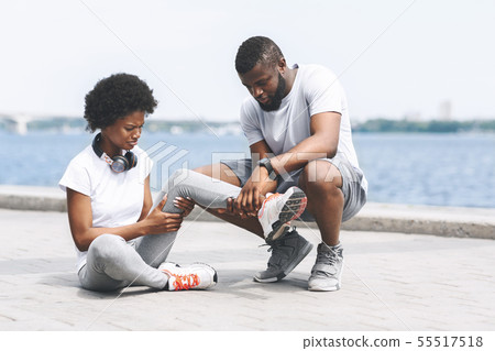 African American Man Examining Woman's Sprained Ankle Near River 55517518