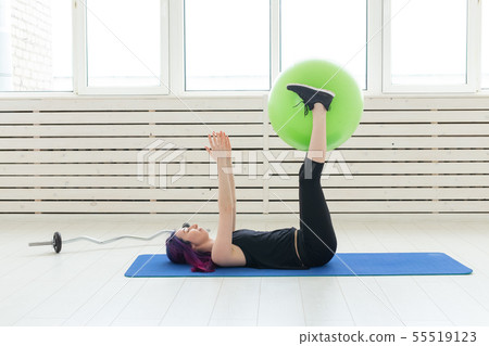 Young slim girl does exercise and stretching on a green fitball In the bright gym. Healthy back and 55519123