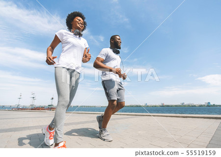 Cheerful Afro Couple Running Along River Bank In City, Low-Angle Shot Cheerful Afro Couple Running Along River Bank In City, Low-Angle Shot 55519159