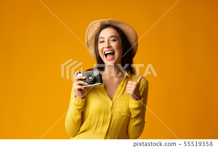 Toursit Girl With Retro Camera Gesturing Thumb Up. Yellow Background Toursit Girl With Retro Camera Gesturing Thumb Up. Yellow Background 55519358