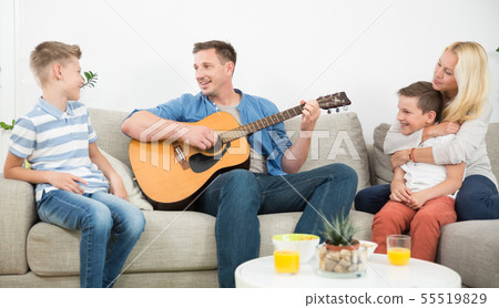 Happy caucasian family smiling, playing guitar and singing songs together at cosy modern home Happy caucasian family smiling, playing guitar and singing songs together at cosy modern home 55519829