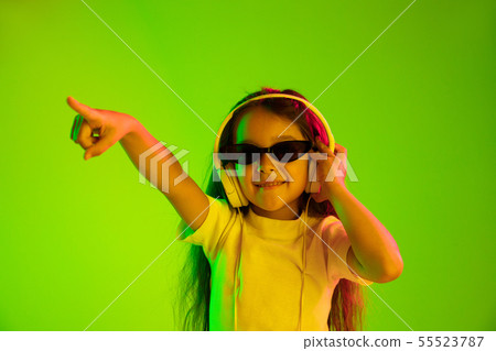 Portrait of little girl in headphones on green background in neon light 55523787
