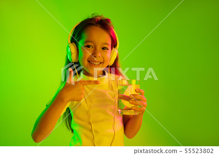 Portrait of little girl in headphones on green background in neon light Portrait of little girl in headphones on green background in neon light 55523802