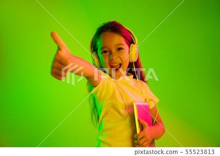 Portrait of little girl in headphones on green background in neon light Portrait of little girl in headphones on green background in neon light 55523813