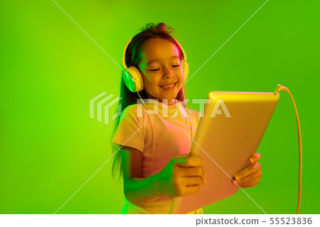 Portrait of little girl in headphones on green background in neon light Portrait of little girl in headphones on green background in neon light 55523836