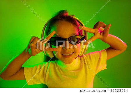 Portrait of little girl in headphones on green background in neon light Portrait of little girl in headphones on green background in neon light 55523914