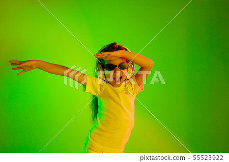 Portrait of little girl in headphones on green background in neon light 55523922