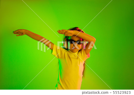 Portrait of little girl in headphones on green background in neon light 55523923
