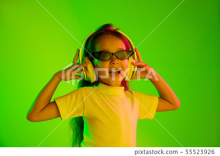 Portrait of little girl in headphones on green background in neon light 55523926