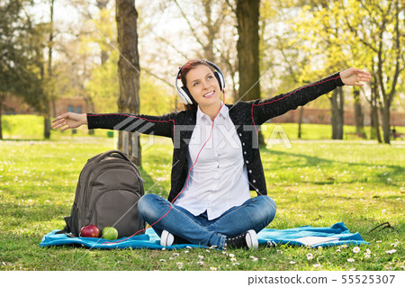 Student in a park with arms outstretched as if 55525307
