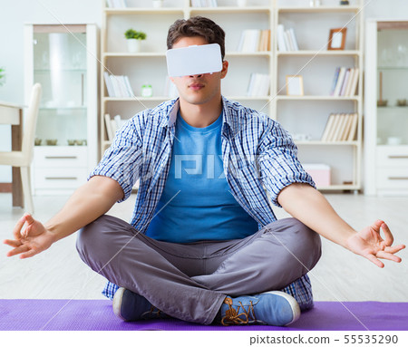 Man wearing virtual reality VR glasses meditating on floor at ho Man wearing virtual reality VR glasses meditating on floor at ho 55535290