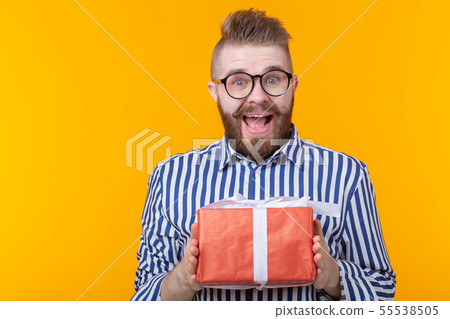 Surprised young hipster man with mustache and beard in surprise unpacks a red box with gifts on a Surprised young hipster man with mustache and beard in surprise unpacks a red box with gifts on a 55538505