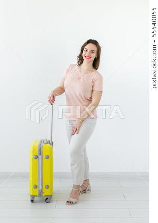Joyful smiling young brunette woman posing with a yellow suitcase while waiting for a vacation. The Joyful smiling young brunette woman posing with a yellow suitcase while waiting for a vacation. The 55540055
