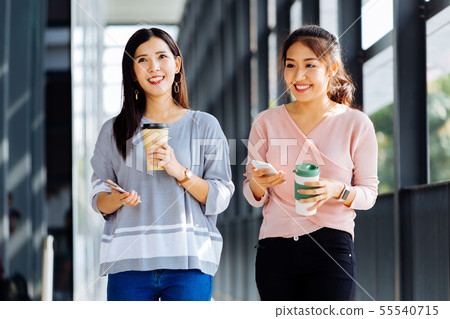 Young Asian business women talking while walking in office building in casual wear Young Asian business women talking while walking in office building in casual wear 55540715