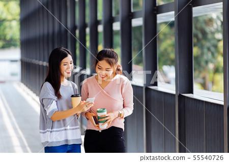 Young Asian business women talking and showing phone screen in office building in casual wear Young Asian business women talking and showing phone screen in office building in casual wear 55540726