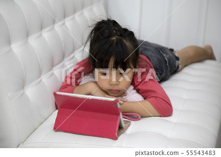 Cute Asian girl laying on sofa and watching taplet Cute Asian girl laying on sofa and watching taplet 55543483