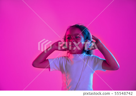 Portrait of little girl in headphones on purple gradient background in neon light Portrait of little girl in headphones on purple gradient background in neon light 55548742