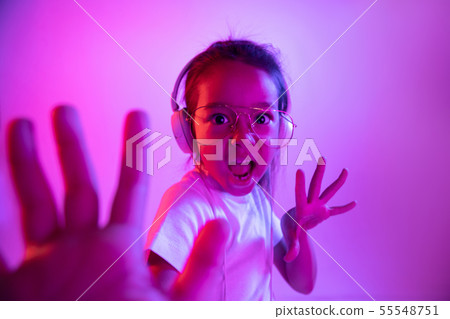 Portrait of little girl in headphones on purple gradient background in neon light Portrait of little girl in headphones on purple gradient background in neon light 55548751