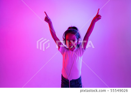 Portrait of little girl in headphones on purple gradient background in neon light 55549026